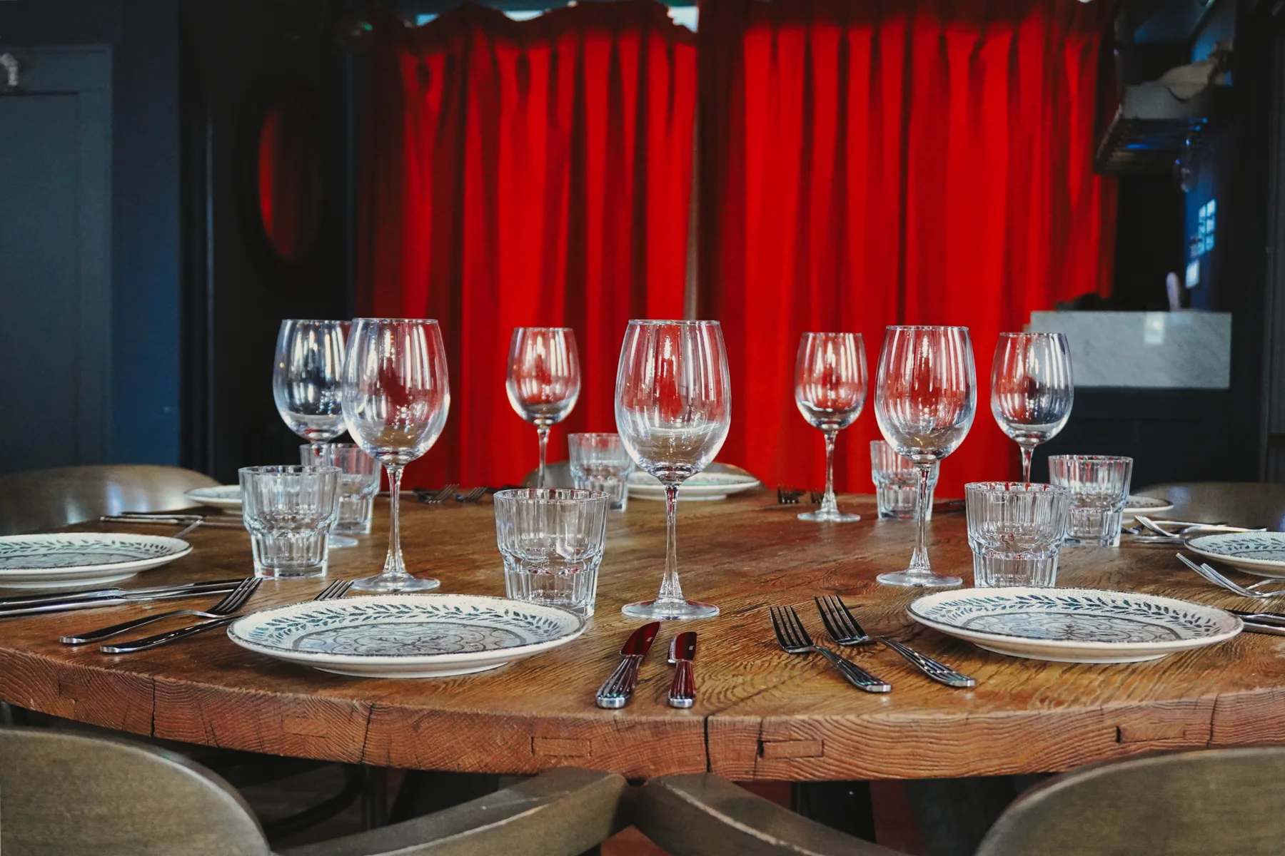 A table set with patterned plates and glassware beside red curtains