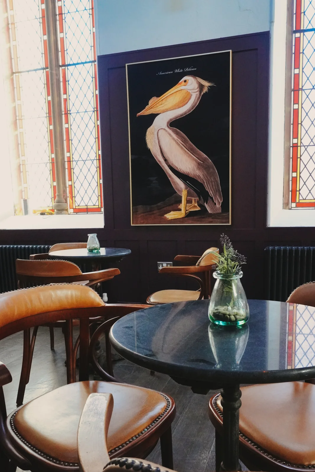 Bird artwork and round tables beside stained-glass windows