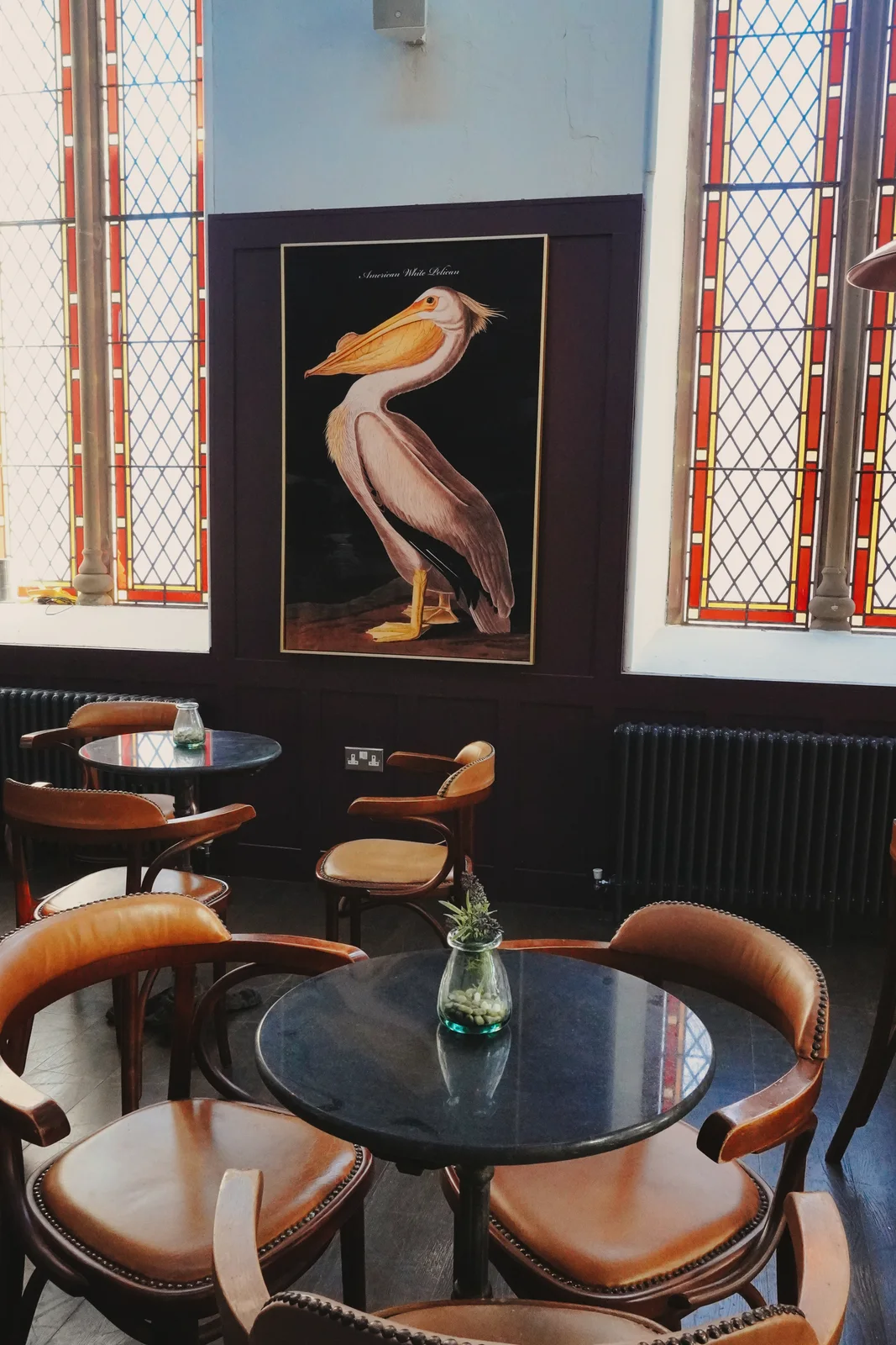 Bird artwork and round tables beside stained-glass windows