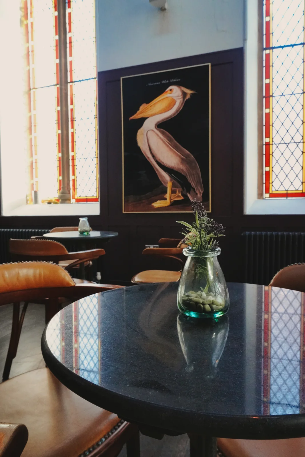 Bird artwork and round tables beside stained-glass windows