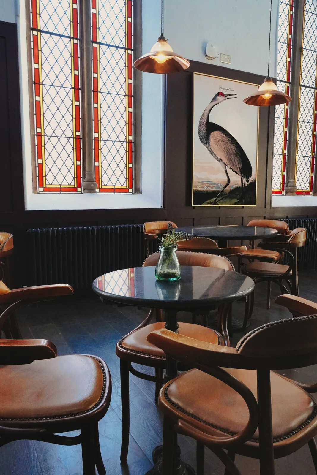 Bird artwork and round tables beside stained-glass windows