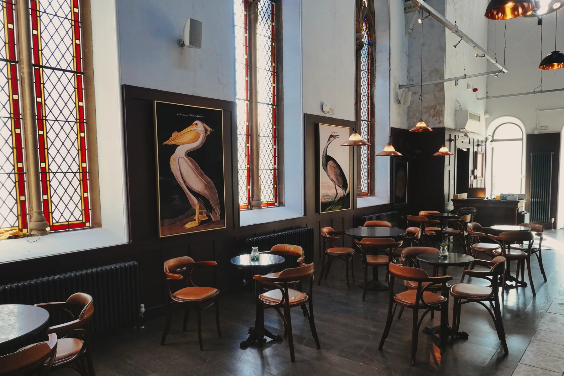 Round tables and bird artwork beneath the stained-glass windows
