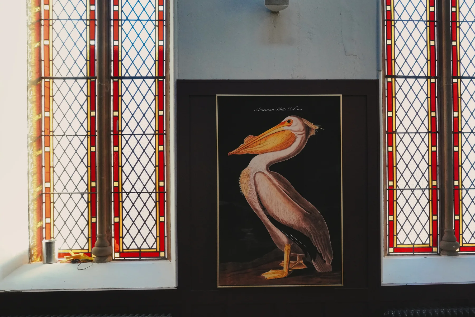 Bird artwork and round tables beside stained-glass windows