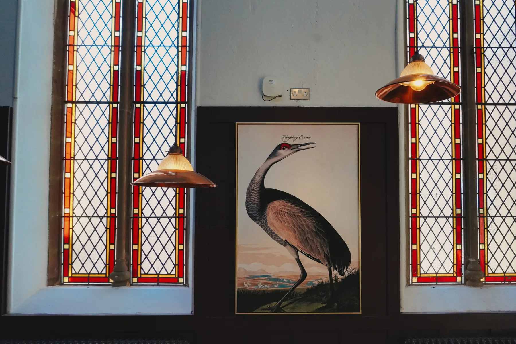 Bird artwork and round tables beside stained-glass windows