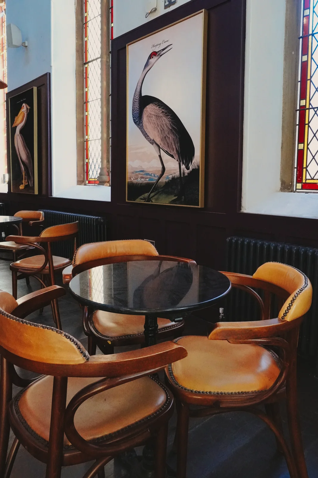 Bird artwork and round tables beside stained-glass windows
