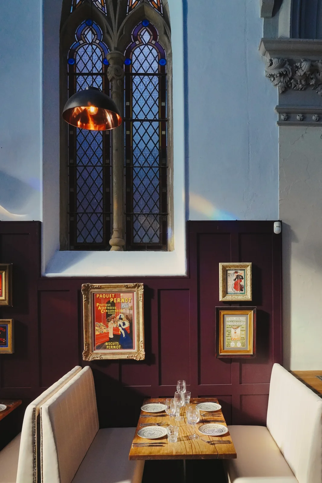 An intimate table beneath a stained-glass window and framed artwork